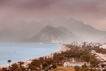 Wall Mural - Aerial view of scenic and popular Konyaalti beach in Antalya resort town. Majestic mountains with haze in the background. Vacation and holiday in Turkiye