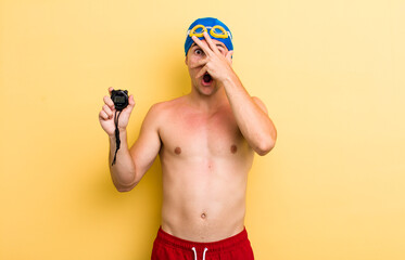 Wall Mural - young handsome guy looking shocked, scared or terrified, covering face with hand. swimmer concept
