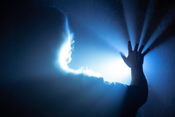 The girl stretches her hand to a source of bright light in the fog, the rays break through her fingers. Mystic atmosphere