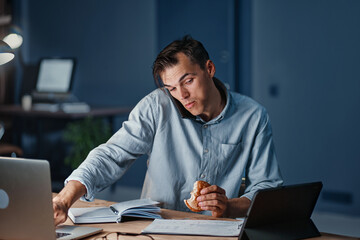 Wall Mural - hungry businessman snacking on a hamburger while working at night.