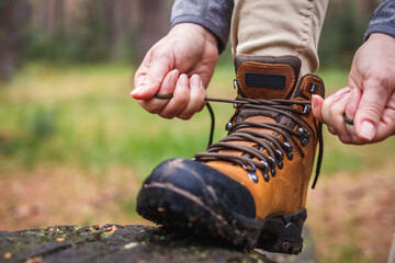 Wall Mural - woman tying shoelace on her hiking boot. tourist is getting ready for hike at forest trekking trail