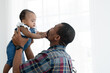 African father with beard playing and carrying his newborn baby girl up in the air and little cute kid have fun to pull dad's beard at home. Relationship of dad and small daughter. White background