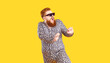 Leinwandbild Motiv Crazy plus size man in funny pajamas dancing and having fun in fashion studio. Happy bearded fat guy wearing cool sunglasses and comfy leopard PJs singing and dancing isolated on yellow background
