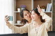 © amnaj - Asian lesbian couple, LGBTQ. Lesbian couple holding smartphone and posing while making selfie together. Happy two young Asia women showing love and romance together at home.