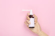Wooden hand holding Throat spray mockup with blank white label for branding or text on pink background. Top view