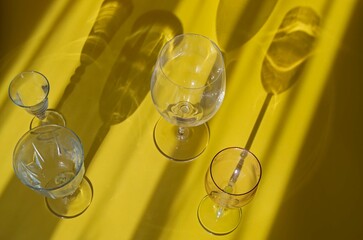 Wall Mural - Abstract composition with different wine glasses on a yellow background with sparkling hard sunny shadows. Layout design, postcard, invitation to a holiday.