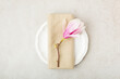 Festive or wedding table setting, porcelain empty plate, napking and cutlery with spring pink magnolia  flowers on beige stone background. Floral elegant decor, top view, flat lay