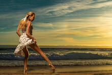 Beautiful Girl Dancing On The Beach Over Sunset Background.