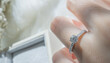 Close up of diamond ring on woman’s finger with  white flower, sunlight and shadow background. Love, valentine, relationship and wedding concept. Soft and selective focus.