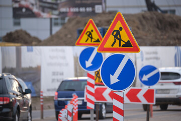 Roadworks warning traffic signs of construction work on city street and slowly moving cars