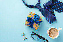 Father's Day Concept. Top View Photo Of Polka Dot Giftbox With Blue Ribbon Bow Cup Of Coffee Glasses Cufflinks And Blue Tie On Isolated Pastel Blue Background