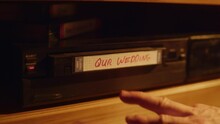 Close Up Of A Person Inserting A VHS Cassette In A Player With Nostalgic Wedding Footage From Home Video Camera. Retro Nineties Technology Concept. Old VCR Shot With Shallow Depth Of Field And Bokeh.