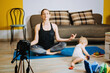 © irissca - Young mother fitness instructor personal trainer record video near camera at home with baby daughter