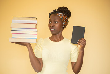 Wall Mural - young woman comparing printed books to e-book while frowning at books on her right hand and e-book on her left hand 