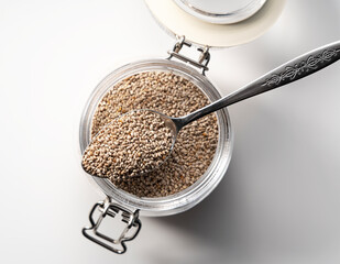 Wall Mural - Glass container with spoon and white chia seeds placed on white background.