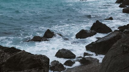 Wall Mural - Turquoise sea stone beach, breaking waves on a cloudy spring day. Beautiful sea background. The concept of summer, vacation, travel. The purest clear sea water, large stones on the beach close-up