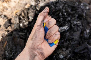 the symbol of ukraine is clutched in the hand against the background of coals from the conflagration. ukraine on fire, struggle for freedom in ukraine. yellow blue ribbon of the flag of ukraine