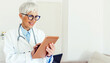 © Jelena Stanojkovic - Cropped shot of an attractive mature female doctor using her tablet while standing in the office. Mature healthcare worker standing at doctor's office and working on tablet.