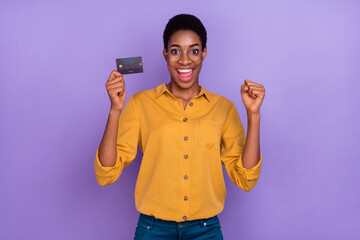 Portrait of attractive brunet cheery trendy skilled girl holding atm card rejoicing isolated over violet purple color background