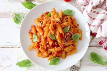 Penne pasta with tomato sauce, parmesan cheese and pasil on wooden table. Top view.