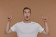 © timtimphoto - Indoor portrait of young blonde man posing over beige background points with fingers upwards with shocked facial expression
