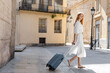 © LIGHTFIELD STUDIOS - young woman with long red hair walking with suitcase on street in valencia.
