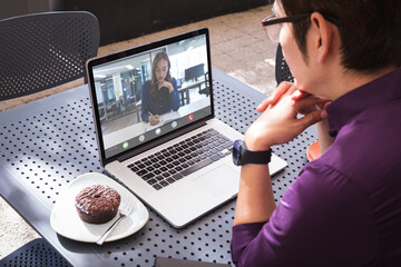 Sticker - Caucasian businesswoman writing on book during video call with asian male colleague sitting in cafe