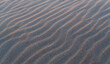 Sand ripples texture with waves at sunset as background or wallpaper.