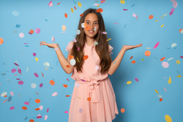 Wall Mural - Portrait of a happy beautiful girl standing under confetti rain and celebrating isolated over blue background