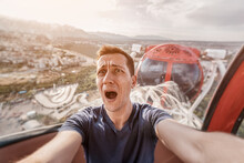 A Guy With Acrophobia Or Fear Of Heights Screams With Funny Emotions On His Face From The View From A High Ferris Wheel In An Amusement Park