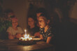 Cute child girl at table with birthday cake with siblings, dark style. Cake and candle 9 years birthday celebration