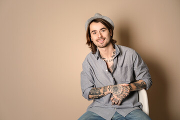 Young man with tattoos on body against beige background