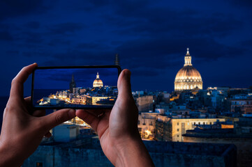 Sticker - Tourist taking photo of illuminated at night Valletta old town and harbor in Valletta, Malta.