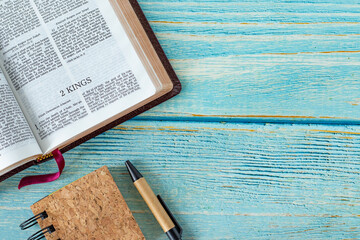 Wall Mural - 2 Kings open Holy Bible Book with a notebook and pen on a wooden background with copy space. Top table view. Old Testament Scripture study, biblical concept.