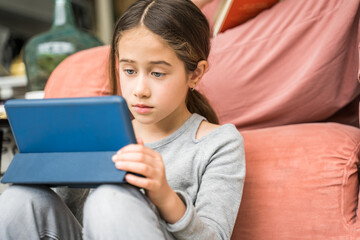 Teenage girl sitting at the floor at home and watching videos at her smartphone