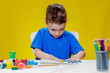 © volody10 - A little preschooler is sitting at a table, drawing with his palms on a sheet of paper. Colorful handprints. Preschooler development