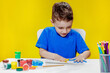 © volody10 - A little preschooler is sitting at a table, drawing with his palms on a sheet of paper. Colorful handprints. Preschooler development