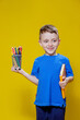 Smiling happy schooler in blue t-shirt holding multicolored pencils and book on yellow background
