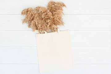 Fall mockup with tote bag blank and dry reeds on white wood background. Sale mock up. Shopping bag, handbag. Ecological concept.