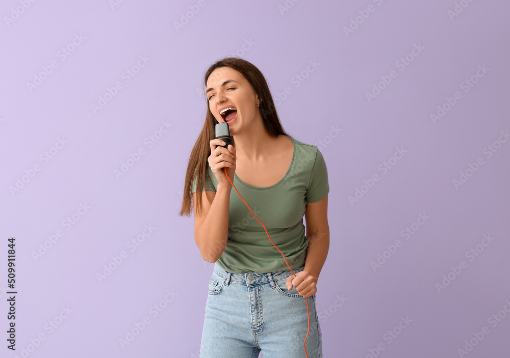 Pretty young woman with microphone singing on lilac background