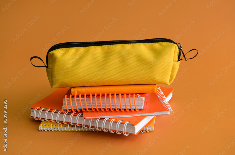Pencil case and notebooks on orange background