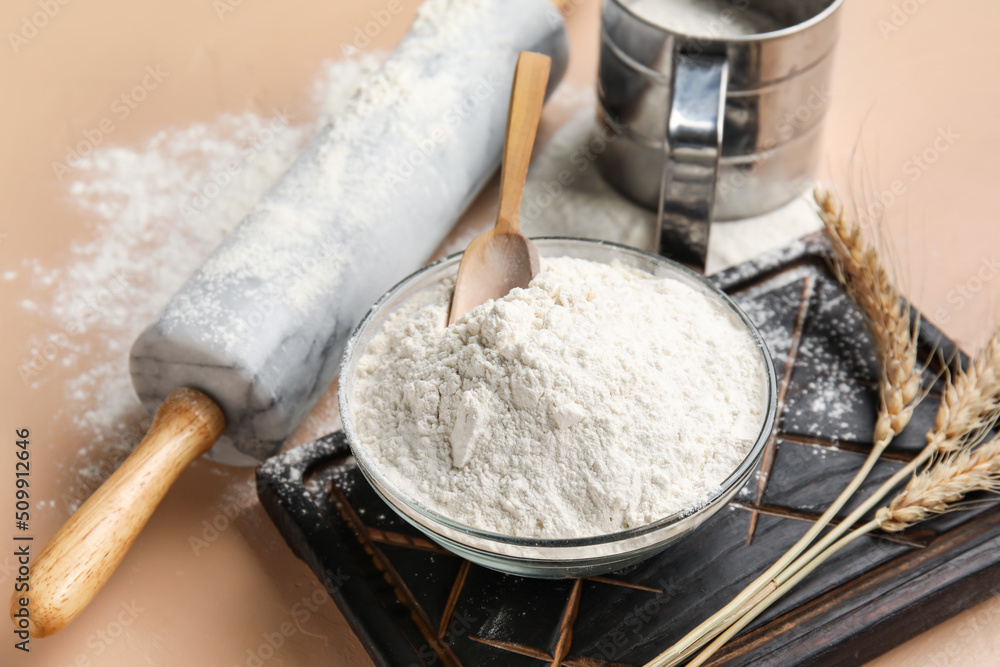 Bowl with wheat flour and utensils on color background, closeup