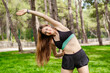 © platinumArt - Happy sportive woman wearing sports bra standing on city park, outdoors exercising before jogging, stretching her muscles, feeling healthy and motivated.