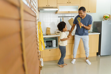 Wall Mural - Happy relaxed black African American Father and his little afro boy dancing while cooking in the kitchen at home.