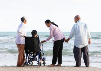 Wall Mural - back view senior woman in a wheelchair with friends enjoy travel on the beach