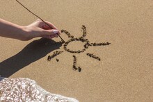Female Hand Draws The Sun On The Sand Near The Sea