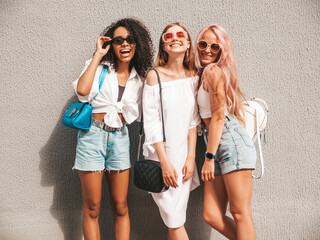Wall Mural - Three young beautiful smiling hipster female in trendy summer clothes.Sexy carefree multiracial women posing on the street background.Positive models having fun