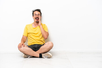 Young caucasian man sitting on the floor isolated on white background with surprise and shocked facial expression