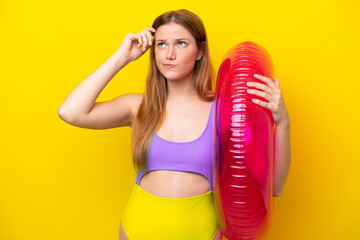 Wall Mural - Young caucasian woman holding air mattress isolated on yellow background having doubts and with confuse face expression