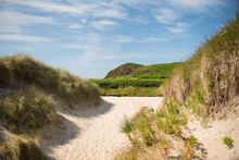 A White Sand Beach Flanked By Vegetation Leading To A Hill Covered In Grass Under A Blue Sky With Clouds In Camusdarach Beach, Mallaig, Scottish Highlands, UK